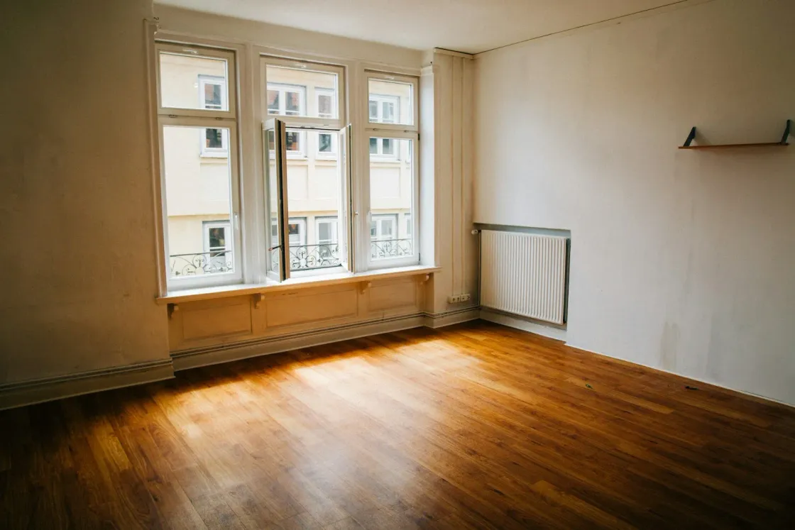 Leeres Altbauzimmer mit Heizkörper unter dem Kastenfenster – im Bestand entscheiden Baujahr und Heizung über die GEG-Pflichten