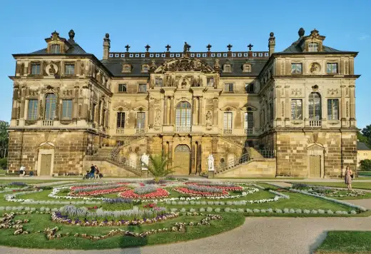Barockes Palais im Großen Garten Dresden mit kunstvoll angelegtem Blumenparterre im Vordergrund unter blauem Sommerhimmel, prägendes Wahrzeichen der Parkanlage am Rande des Stadtteils Gruna.