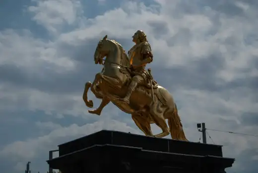 Der Goldene Reiter, das vergoldete Reiterstandbild Augusts des Starken mit steigendem Pferd, leuchtet in warmem Gold vor blauem Wolkenhimmel im Barockviertel der Inneren Neustadt in Dresden.