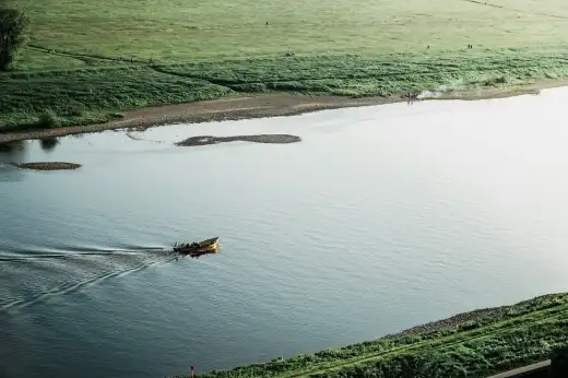 Ruhiges Elbufer mit weiten grünen Elbwiesen, heller Kiesbank und einem kleinen Boot auf dem Wasser – charakteristische Uferlandschaft der Elbe in Dresden, wie sie den Stadtteil Pieschen prägt.
