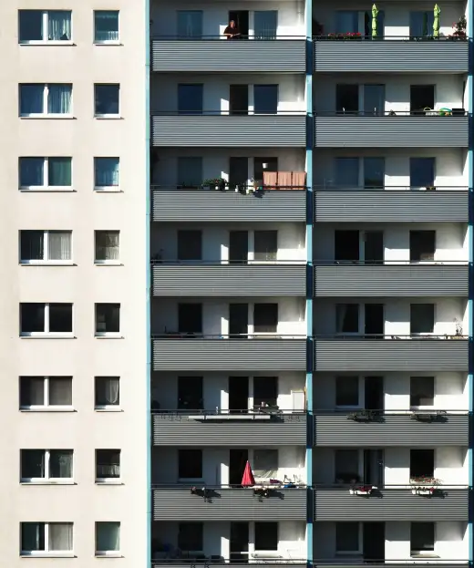 Sanierter Plattenbau-Wohnblock im warmen Sonnenlicht mit langen Balkonreihen und bepflanzten, belebten Balkonen – typische DDR-Wohnbebauung wie im Dresdner Stadtteil Prohlis.