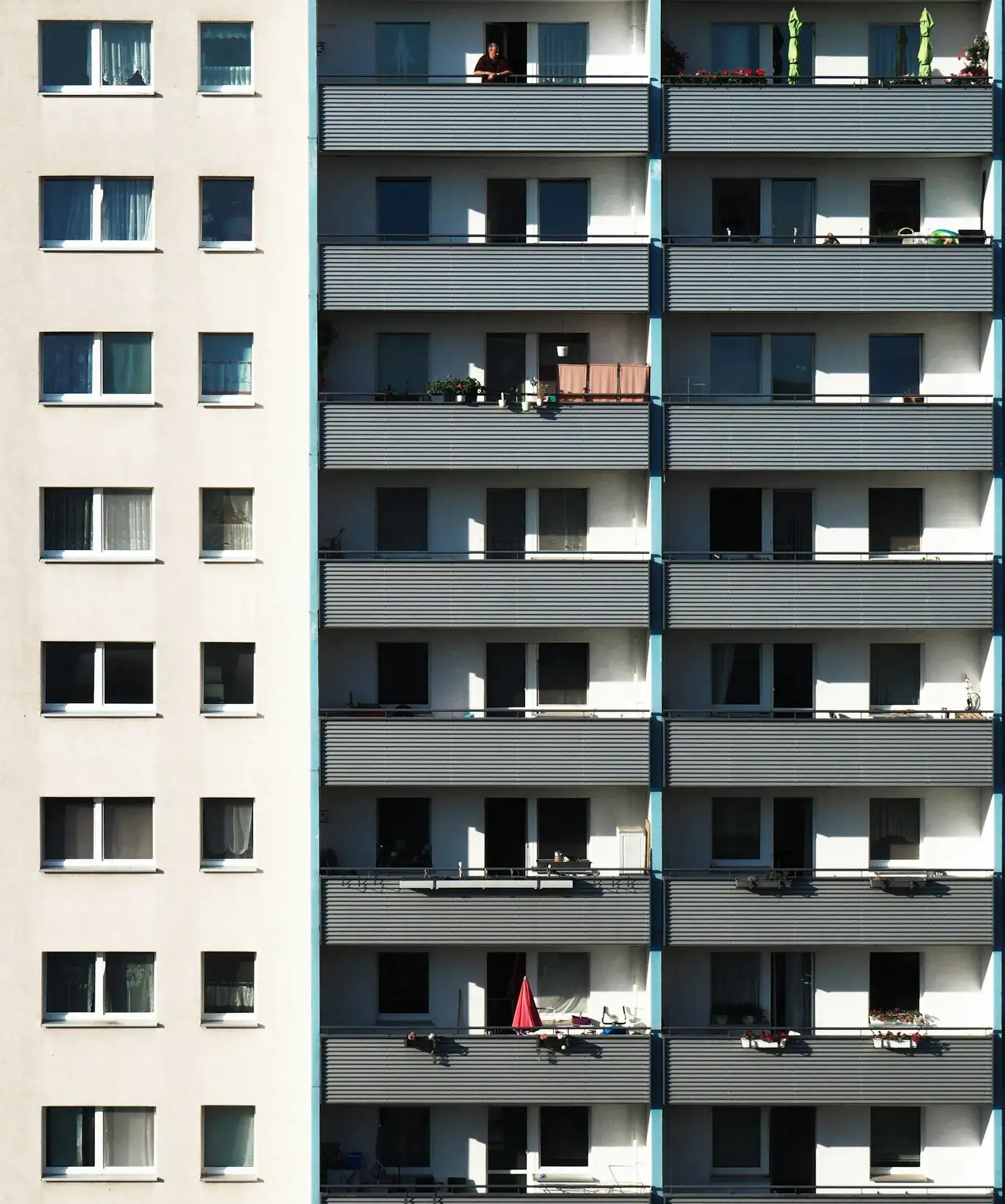 Sanierter Plattenbau-Wohnblock im warmen Sonnenlicht mit langen Balkonreihen und bepflanzten, belebten Balkonen – typische DDR-Wohnbebauung wie im Dresdner Stadtteil Prohlis.