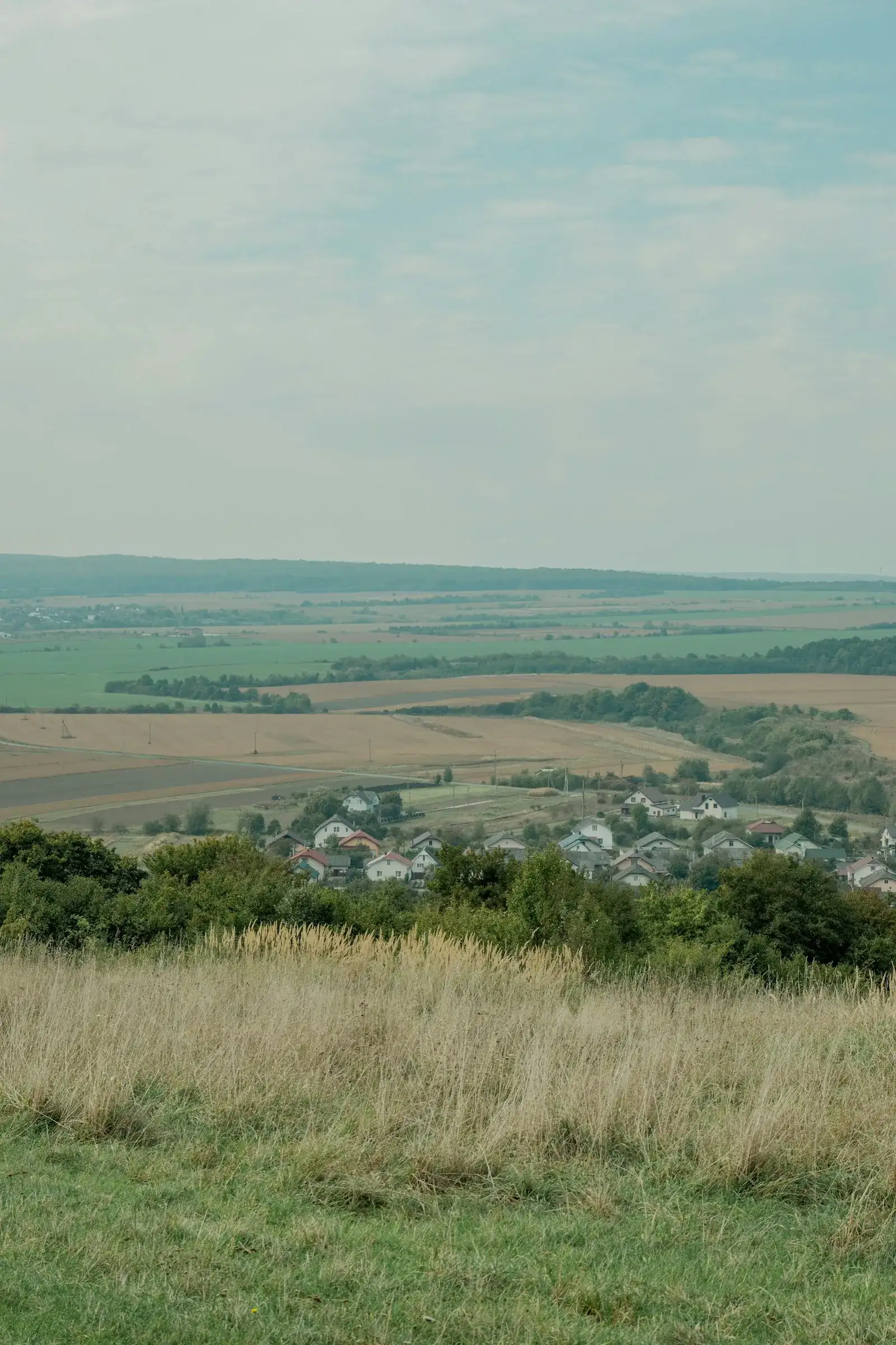 Kleines Dorf am Rand weiter grüner und goldener Felder, dahinter sanft gewellte Agrarlandschaft bis zum Horizont – ländliche Szenerie wie im Schönfelder Hochland östlich von Dresden.
