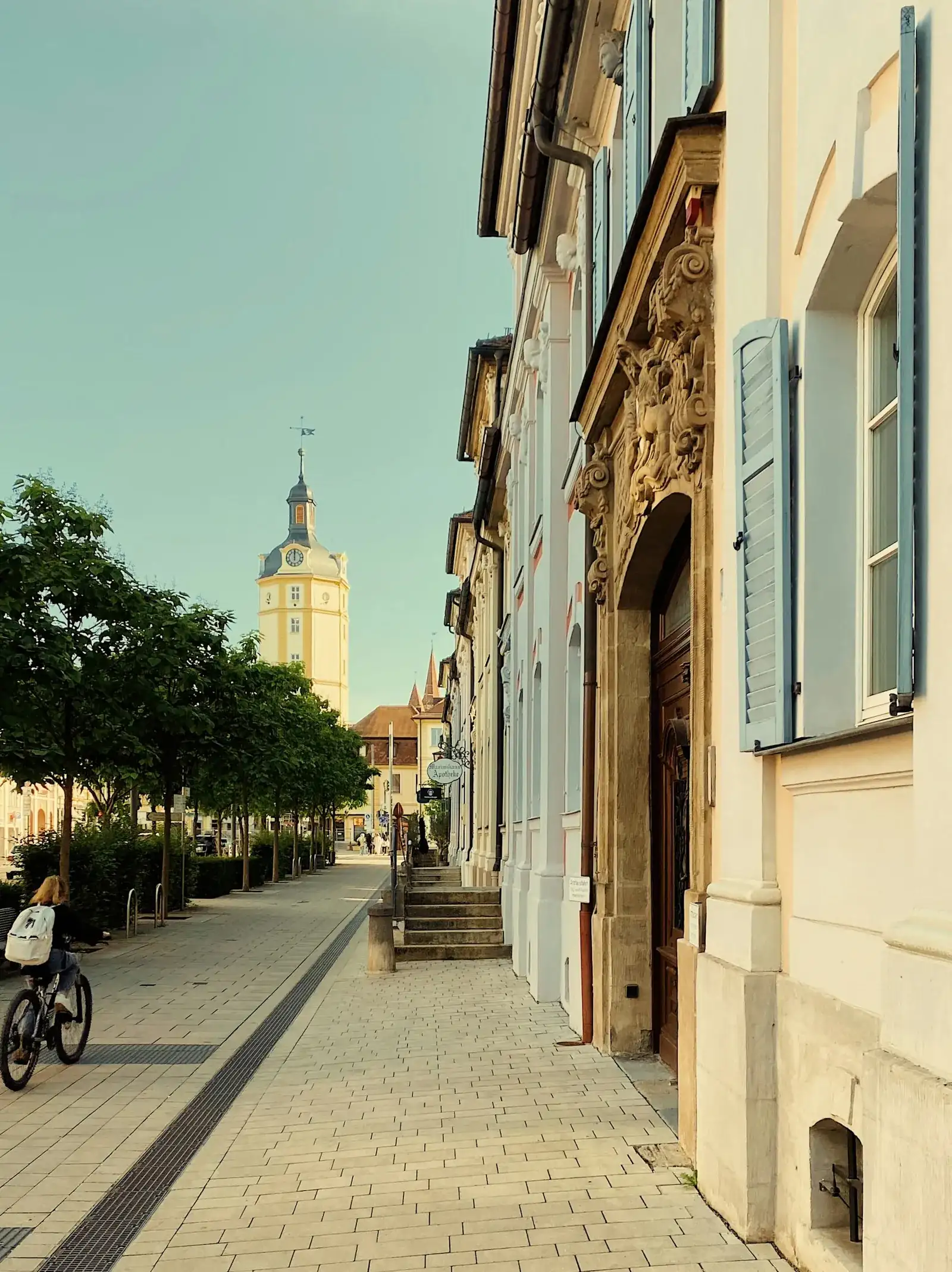 Sonnendurchflutete historische Wohnstraße mit Radfahrerin, hellen Altbaufassaden mit blauen Fensterläden und blauem Himmel – sinnbildlich für das lebendige, studentisch geprägte Straßenbild der Dresdner Südvorstadt rund um die TU Dresden.