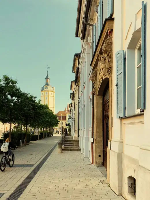 Sonnendurchflutete historische Wohnstraße mit Radfahrerin, hellen Altbaufassaden mit blauen Fensterläden und blauem Himmel – sinnbildlich für das lebendige, studentisch geprägte Straßenbild der Dresdner Südvorstadt rund um die TU Dresden.
