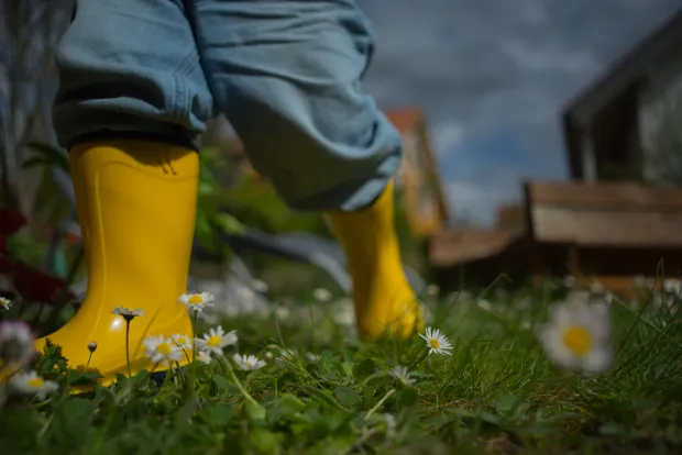 Kind in gelben Gummistiefeln auf einer Blumenwiese – das Kindeswohl bestimmt die Wohnlösung nach der Trennung mit